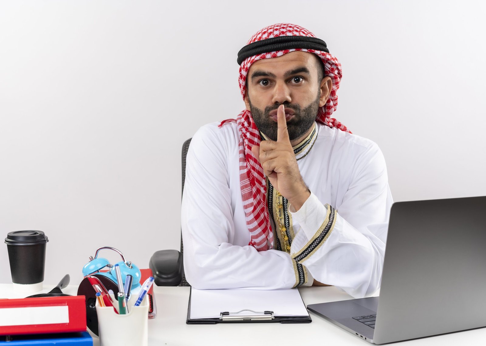 arabic businessman traditional wear sitting table with laptop computer making silence gesture with finger lips working office 1 scaled 1
